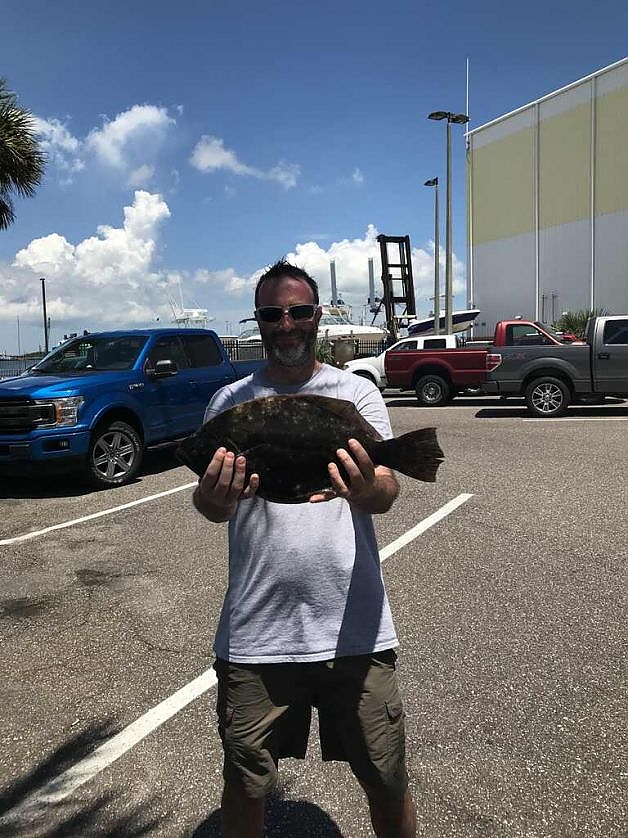 Man in parking lot holds up fish caught on trip